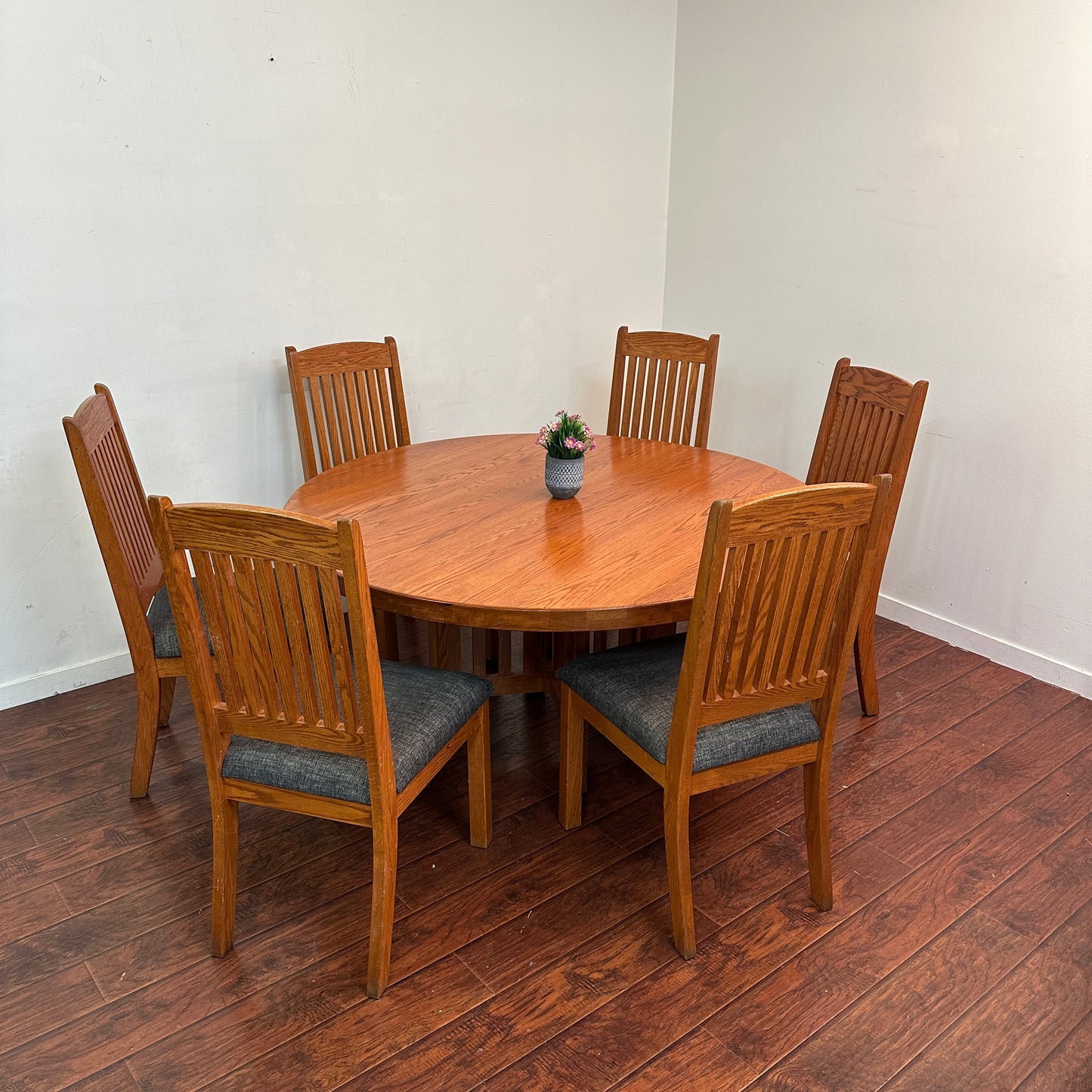 Wooden dining table with six chairs on a wooden floor against a white wall.