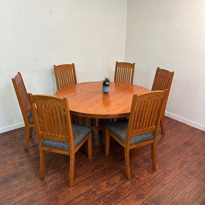 Wooden dining table with six chairs on a wooden floor against a white wall.